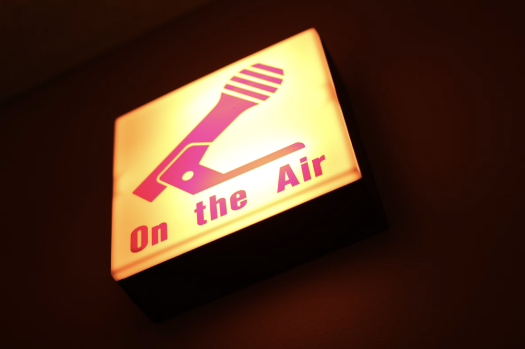 Cartoon of red microphone on a yellow background with the text 'On the Air'